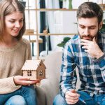 A couple discussing Evansville home insurance options while holding a small wooden house model