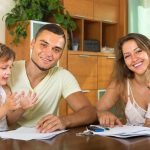 A smiling Wisconsin family sitting together at a table reviewing documents for the cheapest home insurance Wisconsin.