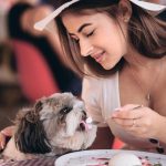 A woman lovingly feeding her small dog at an outdoor café, representing happy pets with pet insurance in Bakersfield.