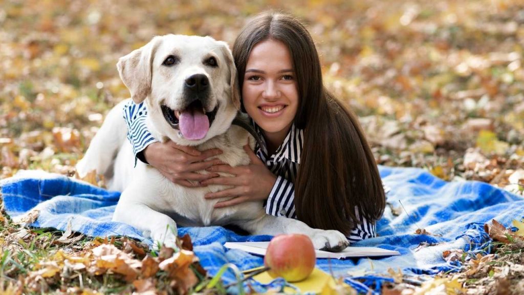 A smiling woman hugging her Labrador dog on a picnic blanket in the park, representing pet happiness and protection with pet insurance in Bakersfield.